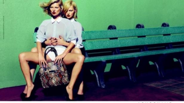 Zwei blonde Frauen sitzen auf einer Parkbank, eine Longchamp-Tasche präsentierend.