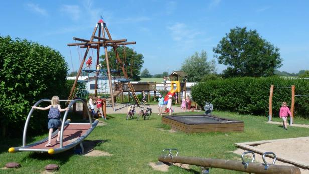 Kinder spielen auf einem sonnigen Spielplatz mit verschiedenen Geräten.