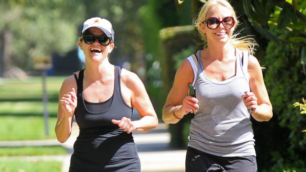 Zwei Frauen joggen lachend an einem sonnigen Tag.