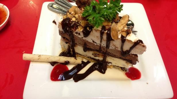 Ein Stück Eistorte mit Schokoladensoße, Mandeln und einer Waffel auf einem Teller.