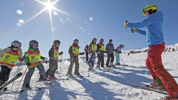 Eine Skigruppe mit Skilehrer auf einer schneebedeckten Piste an einem sonnigen Tag.