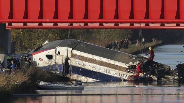 Ein verunglückter Testzug der SNCF liegt unter einer roten Brücke in einem Fluss.