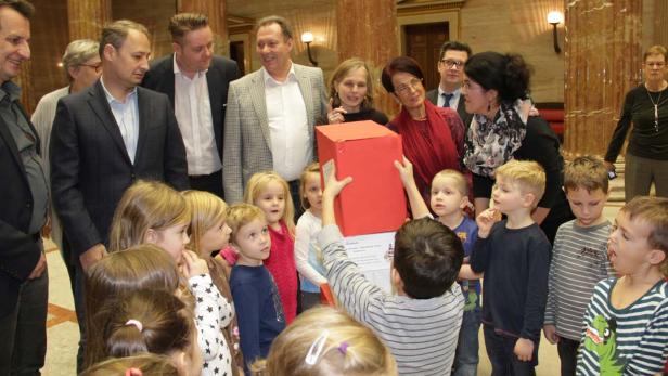 Eine Gruppe von Kindern und Erwachsenen steht um eine rote Kiste herum.