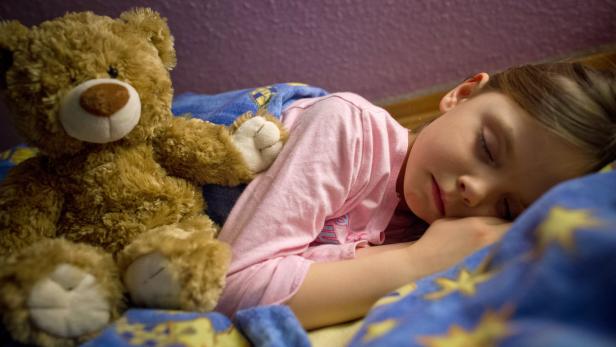 Ein Mädchen schläft mit einem Teddybären im Arm.