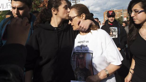 Eine junge Frau küsst eine ältere Frau auf die Stirn, die ein T-Shirt mit der Aufschrift „Protect us from our protectors“ trägt.