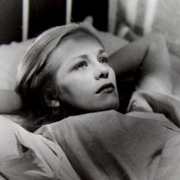 Eine junge Frau liegt in einem Bett und schaut nach oben.