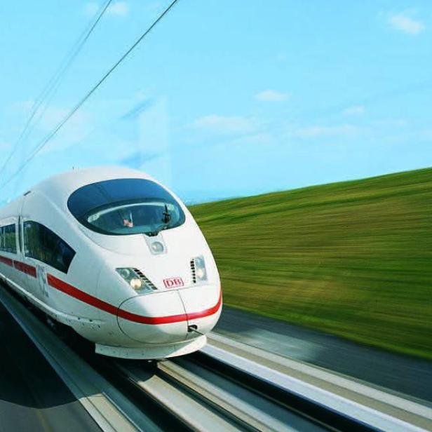 Ein ICE der Deutschen Bahn fährt mit hoher Geschwindigkeit durch eine grüne Landschaft.