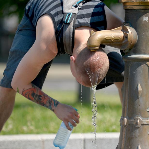 Ein Mann beugt sich über einen Brunnen, um Wasser zu trinken und eine Flasche zu füllen.