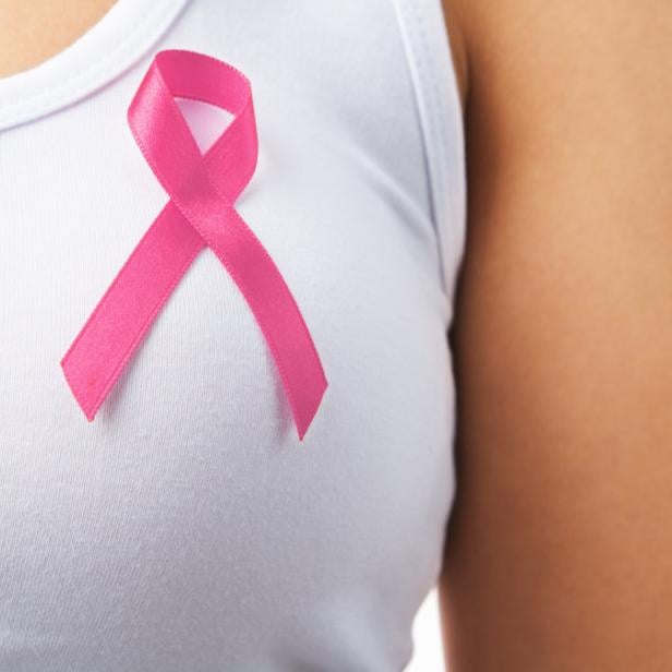 Eine Frau trägt ein weißes Tanktop mit einer rosa Schleife als Zeichen der Brustkrebsvorsorge.