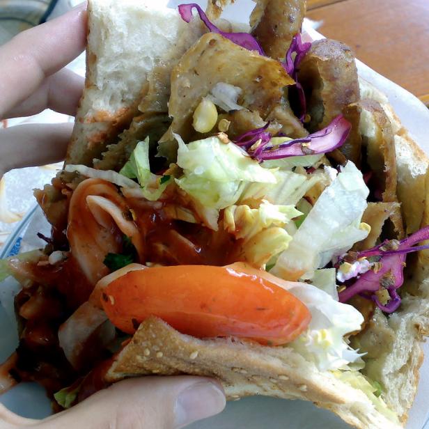 Ein Döner Kebab mit Salat, Fleisch und Soße wird in der Hand gehalten.