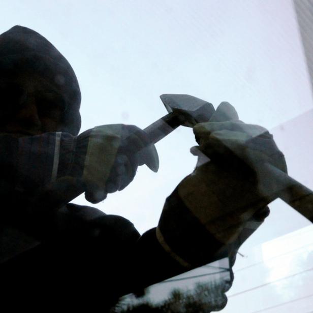 Eine Person mit Kapuze schlägt mit einem Hammer auf eine Scheibe.