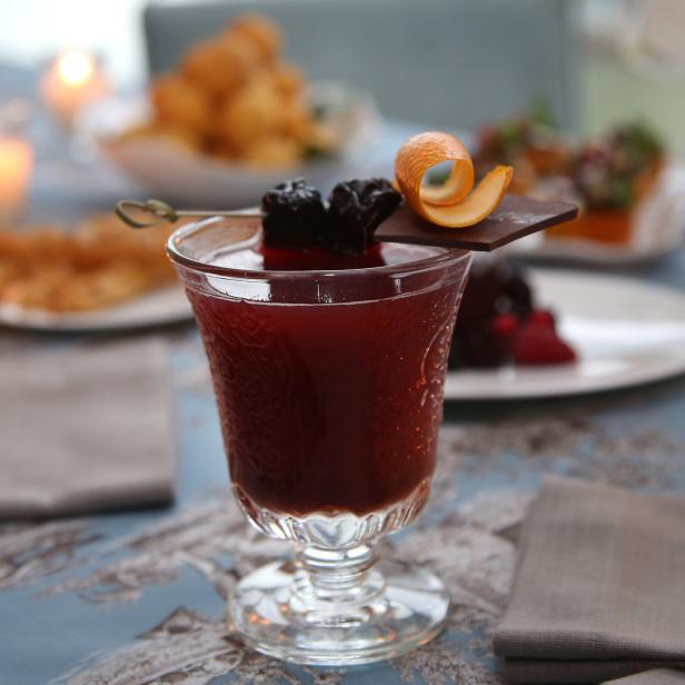 Ein Cocktail mit Brombeeren, Orangenschale und Schokolade auf einem festlichen Tisch.