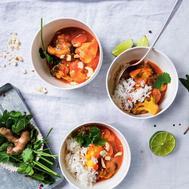 Drei Schalen mit Curry, Reis, Gemüse und Cashewnüssen auf einem weißen Tuch angerichtet.