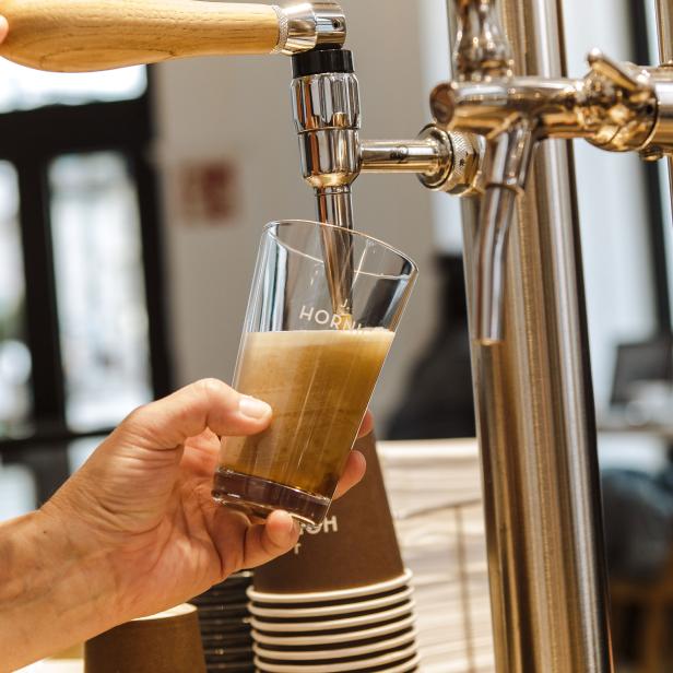 Ein Glas wird mit einem Getränk an einem Hahn befüllt.