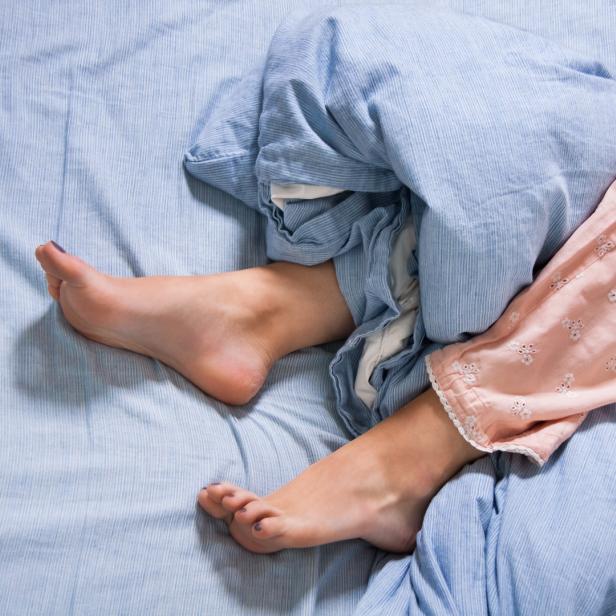 Eine Person liegt mit rosafarbener Schlafanzughose und blauer Bettdecke im Bett.