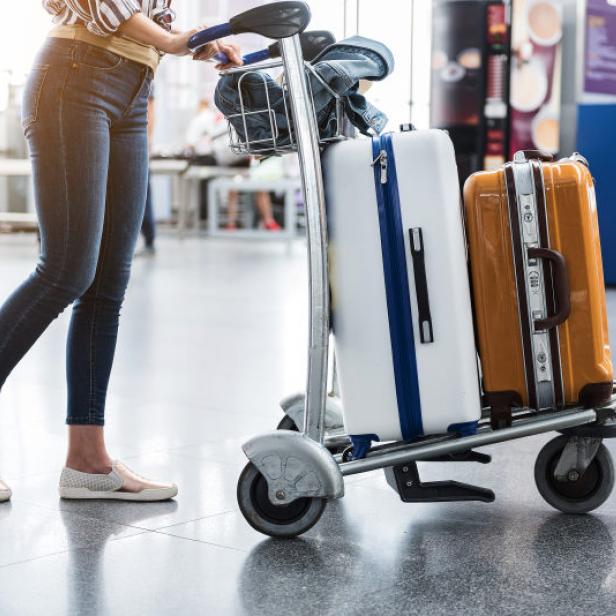 Eine Frau schiebt einen Gepäckwagen mit Koffern durch einen Flughafen.