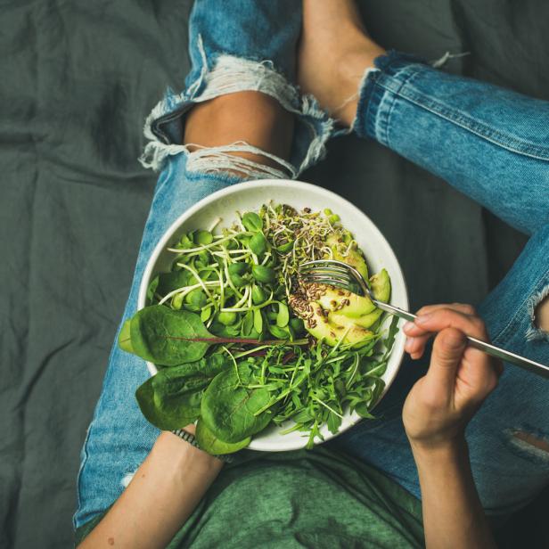 Eine Frau isst einen Salat mit Avocado und Sprossen aus einer Schüssel.