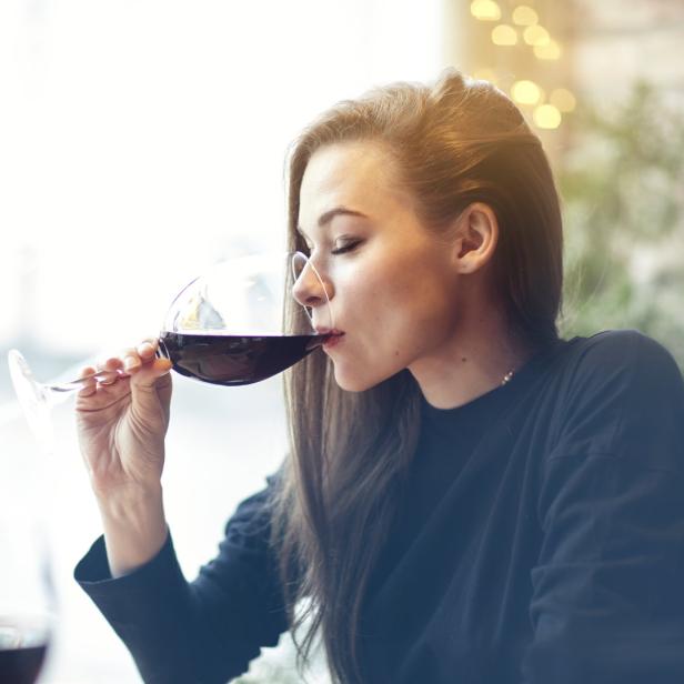 Frau trinkt Rotwein aus langstieligem Glas.