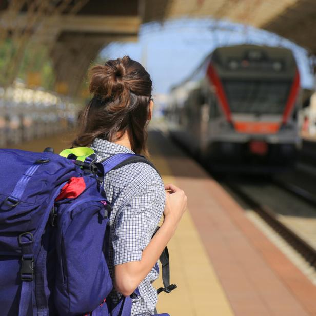 Eine Frau mit Rucksack wartet auf einem Bahnsteig auf den Zug.