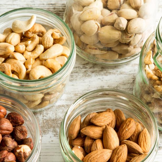 Verschiedene Nüsse wie Mandeln, Haselnüsse, Cashews, Pistazien und Walnüsse in Gläsern.