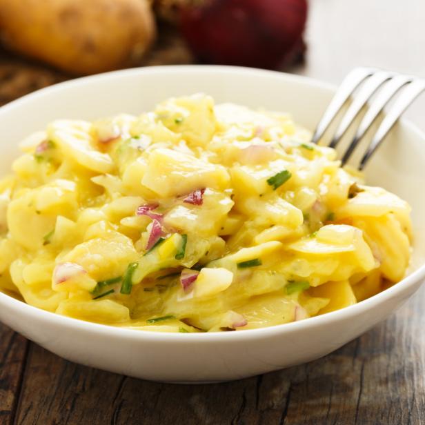 Ein Schüssel Kartoffelsalat mit roten Zwiebeln und Schnittlauch auf einem Holztisch.