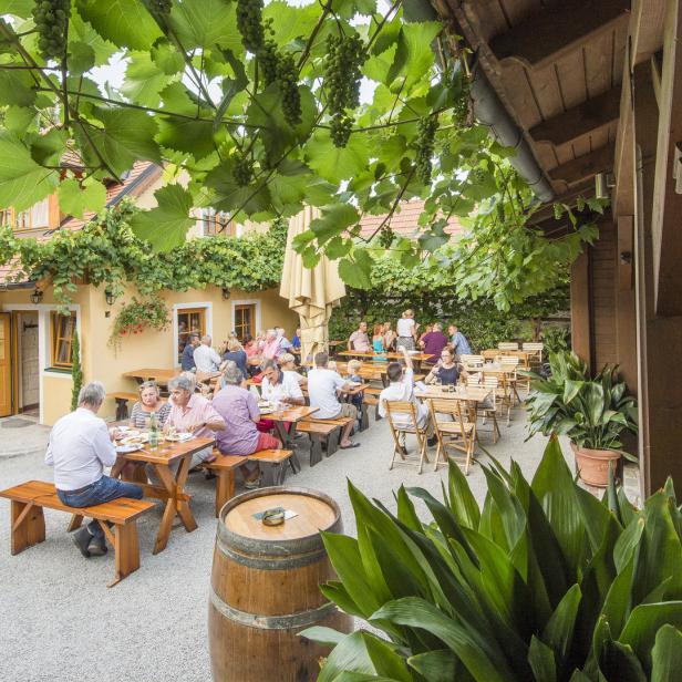 Ein Heuriger mit Gästen, die unter Weinreben sitzen und essen.