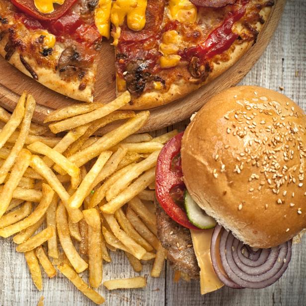 Muffins, Pommes, Burger und eine Pizza stehen auf einem Tisch.
