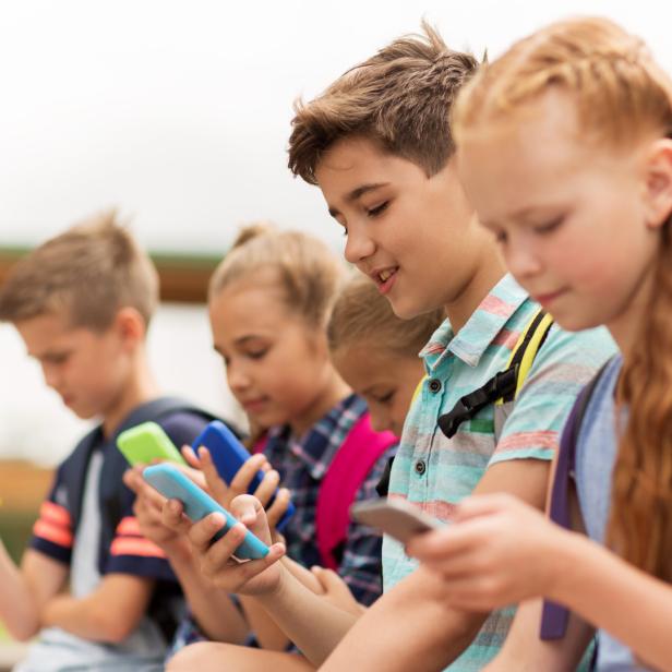 Eine Gruppe von Schulkindern sitzt nebeneinander und benutzt Smartphones.