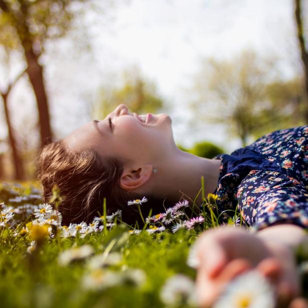 Eine junge Frau liegt auf einer Wiese voller Gänseblümchen und lächelt.