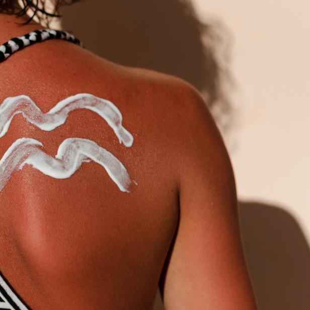Sonnencreme bildet das Sternzeichen Wassermann auf dem Rücken einer Frau.