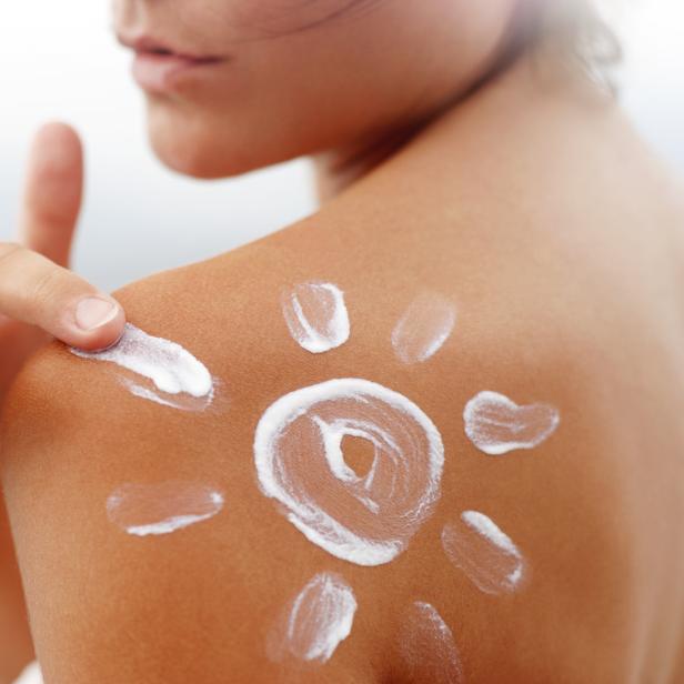 Eine Frau trägt Sonnencreme in Form einer Sonne auf ihrer Schulter auf.