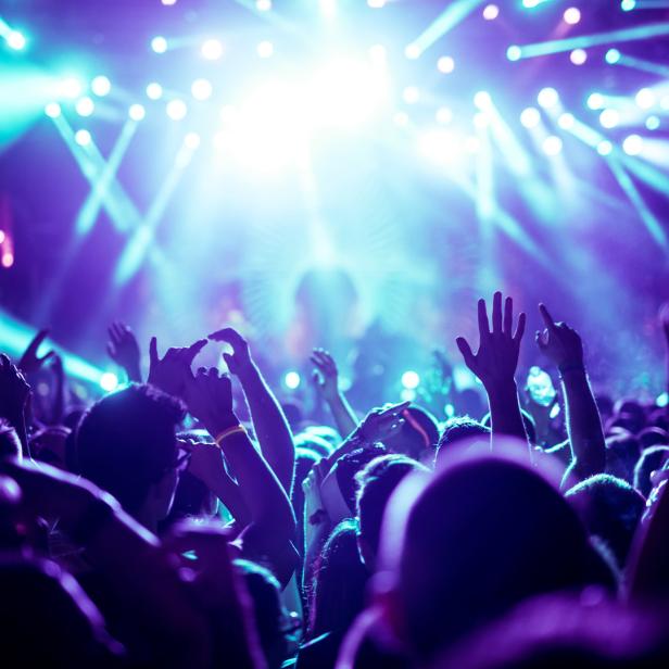 Eine Menschenmenge feiert mit erhobenen Händen auf einem Konzert mit blauem Licht.