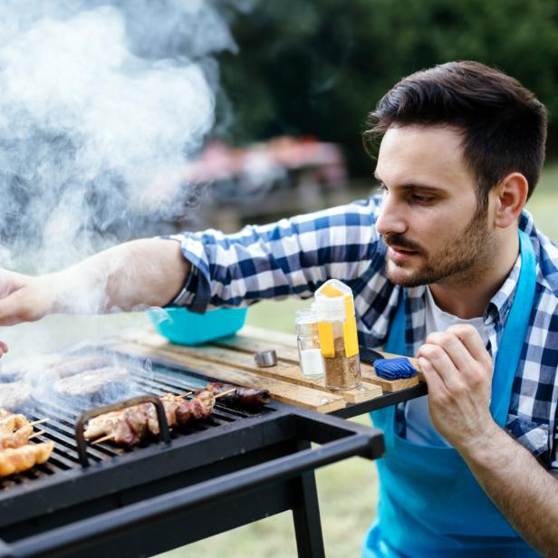 Ein Mann grillt Fleisch und Spieße auf einem Grill.