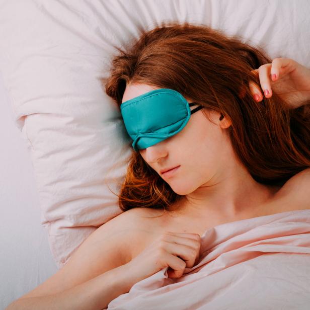 Eine Frau mit Schlafmaske schläft in einem Bett mit rosa Bettwäsche.