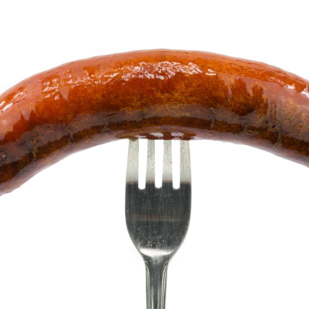 Eine glänzende, gegrillte Wurst auf einer Gabel.