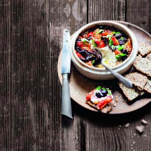 Ein Gericht mit Käse, Tomaten und Oliven wird mit Crackern serviert.