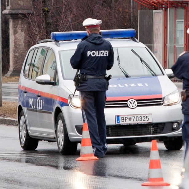 Ein Polizist steht neben einem Polizeiauto auf einer regnerischen Straße.