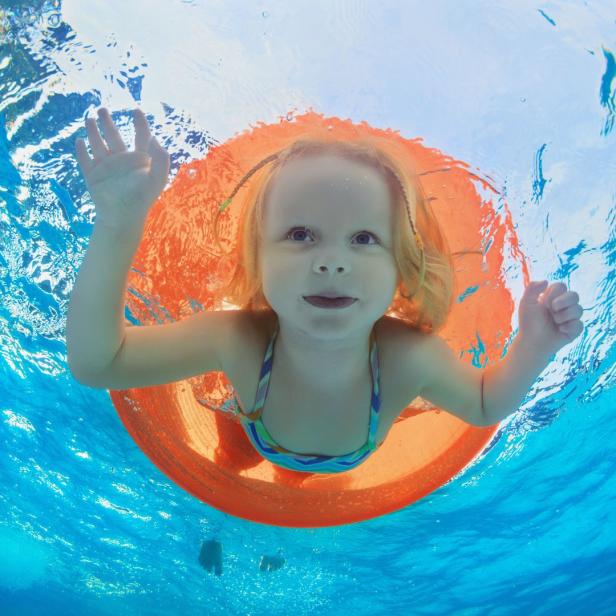 Ein kleines Mädchen schwimmt mit einem orangefarbenen Schwimmreifen im Pool.