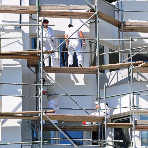 Mehrere Bauarbeiter arbeiten auf einem Gerüst an der Fassade eines Gebäudes.