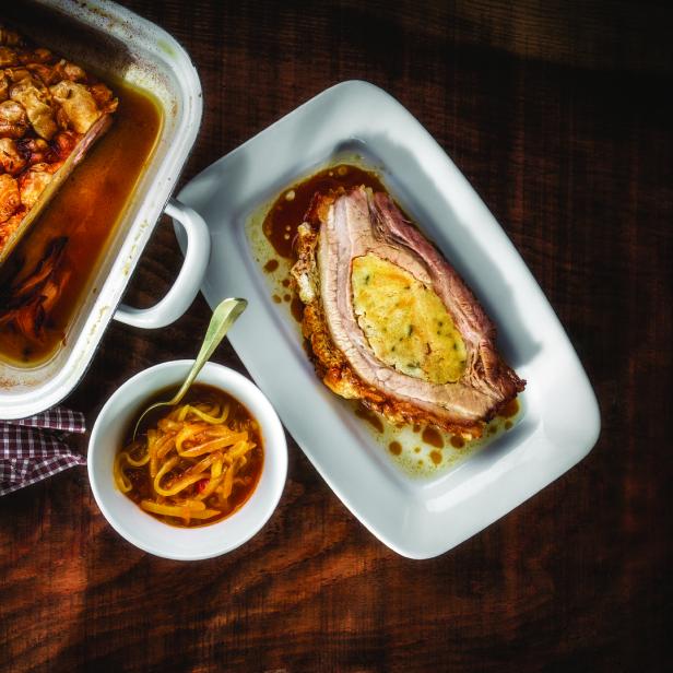 Ein gefüllter Schweinebraten wird mit Soße und Zwiebelringen serviert.