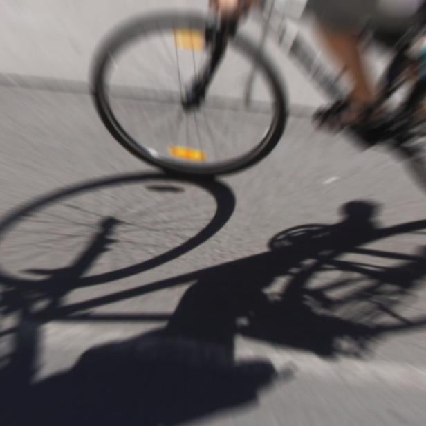 Ein Radfahrer fährt schnell auf einer asphaltierten Straße, sein Schatten ist deutlich sichtbar.