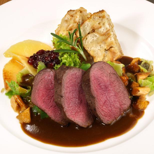 Ein Teller mit gebratenem Hirsch, Semmelknödeln, Preiselbeeren und Pfifferlingen in Soße.