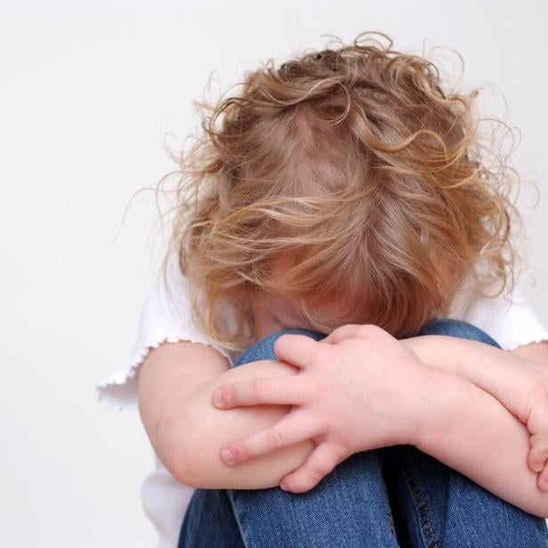 Ein trauriges Kind mit blonden Locken versteckt sein Gesicht in den Armen.