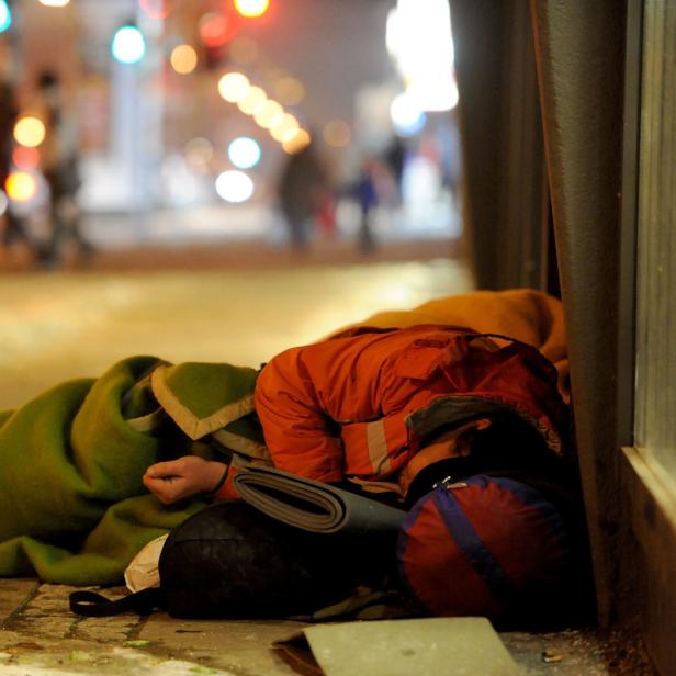 Eine obdachlose Person schläft nachts auf dem Bürgersteig, zugedeckt mit Decken.