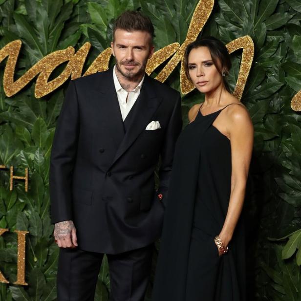 David und Victoria Beckham posieren auf einem roten Teppich vor einer Wand aus Blättern.