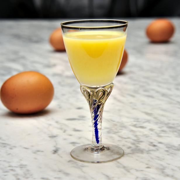 Ein Glas Eierlikör steht auf einem Tisch, umgeben von Eiern.