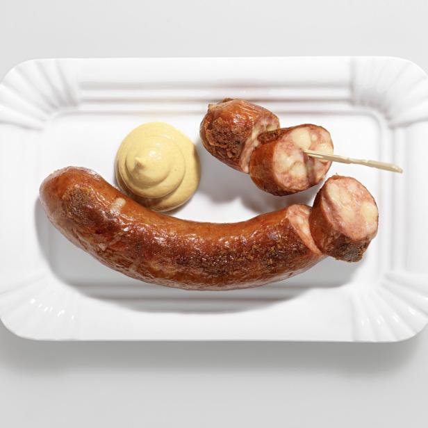 Eine Bratwurst mit Senf auf einem weißen Pappteller.
