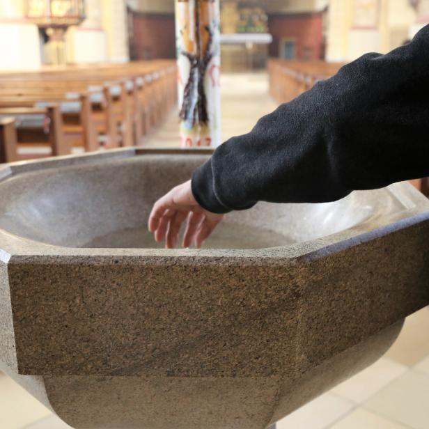 Katholischer Priester fasst ins Taufbecken.