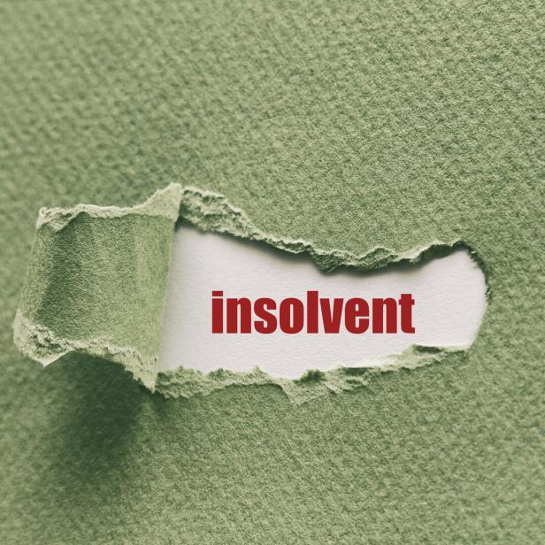 Das Wort „insolvent“ ist durch ein Loch in einem grünen Blatt Papier sichtbar.