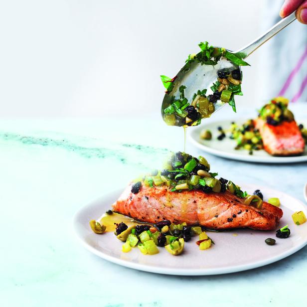 Ein Teller mit Lachs, der mit Oliven, Kapern und Kräutern belegt ist.